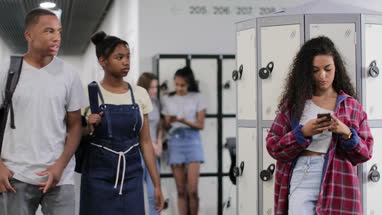 Female student looking at smartphone in high school corridor