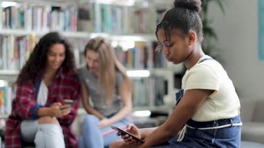 Student alone using smartphone at recess in library
