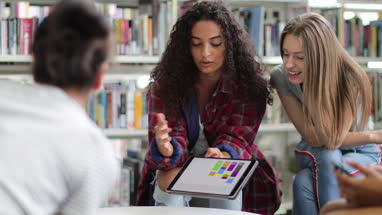 High school students studying together in a library with a digital tablet