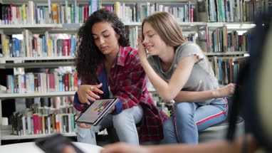 High school students studying together in a library with a digital tablet