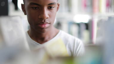 Teen african american boy choosing book in library