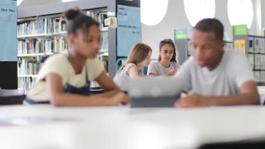 High school students studying together in a library with a digital tablet