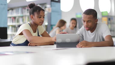 High school students studying together in a library with a digital tablet