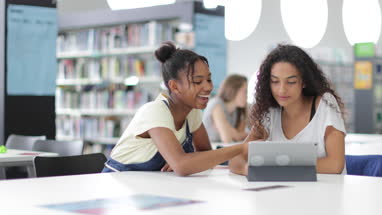 High school students studying together in a library with a digital tablet