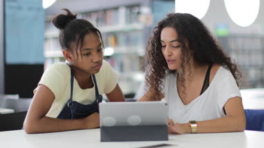 High school students studying together in a library with a digital tablet