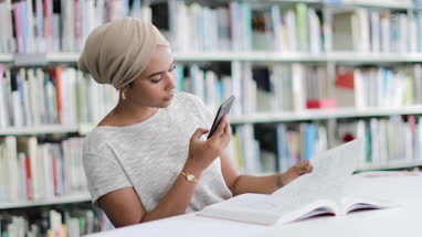Muslim female student in college library using smartphone