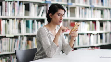 Muslim female student in college library using smartphone