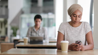 Young adult Muslim female using a smartphone in a cafe