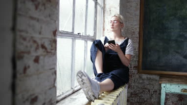 Millennial using smartphone by window in a loft apartment