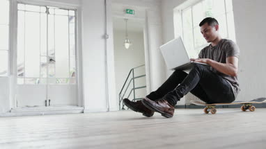Young adult male working on laptop with skateboard