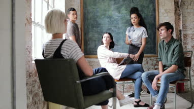 Young adults in a meeting in a creative studio writing on a blackboard 