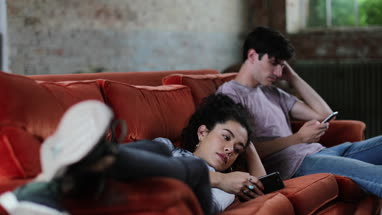 Millennials using smartphones relaxing on sofa