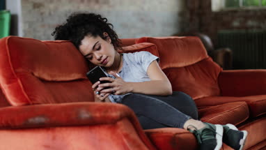 Generation Z female relaxing on sofa using smartphone