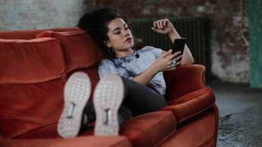 Generation Z female relaxing on sofa using smartphone
