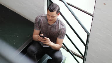 Young adult male using smartphone sitting in stairwell