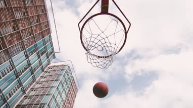 Basketball hoop being scored with view of sky and hi rise