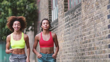 Young adult female friends running together in an urban environment