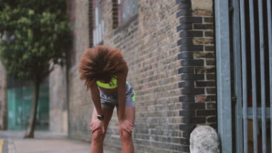 Young adult female checking activity tracker on a run in urban city