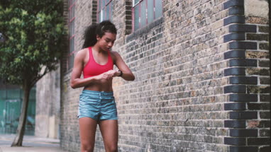 Young adult female checking activity tracker on a run in urban city