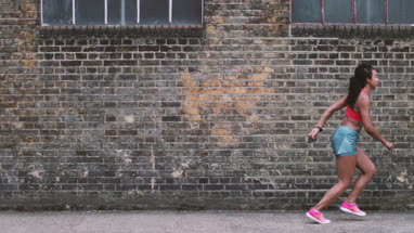 Young adult female leaping in the air with brick wall backdrop