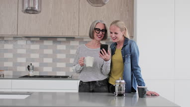 Mature adult woman with grown up daughter looking at smartphone in kitchen