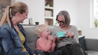 Boy opening a birthday present with grandmother and mother