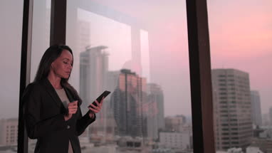 Businesswoman working late using smartphone with city skyline in background