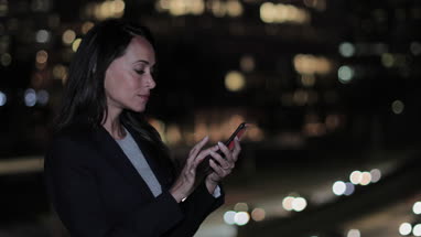 Businesswoman using smartphone outdoors at night