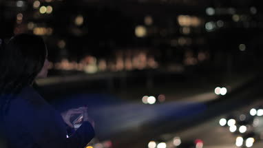 Young adult female taking photo with smartphone of city skyline at night