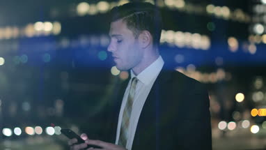 Businessman using smartphone outdoors at night with bokeh effect