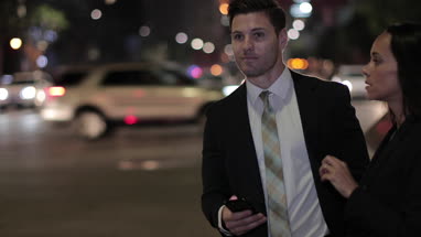 Business executives using an app to book a taxi on street at night
