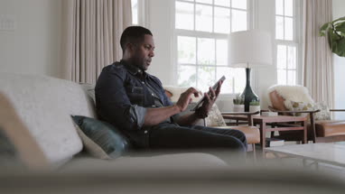 African American adult male using digital tablet at home on sofa