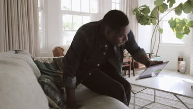 African American adult male using digital tablet at home on sofa