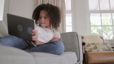 African American girl playing games on digital tablet at home on sofa