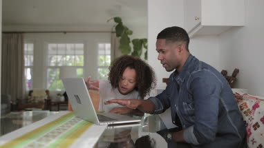 African American father helping daughter with homework using laptop