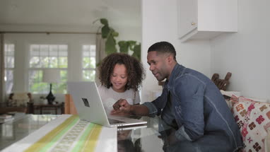 African American father helping daughter with homework using laptop