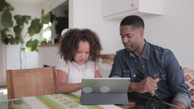 African American father helping daughter with homework using digital tablet