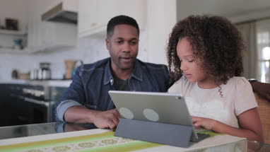 African American father helping daughter with homework using digital tablet