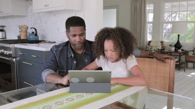 African American father helping daughter with homework using digital tablet