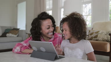African American mother helping daughter with homework using digital tablet