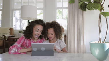 African American mother helping daughter with homework using digital tablet
