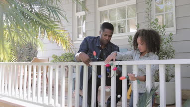 African American father and daughter hanging christmas lights outdoors
