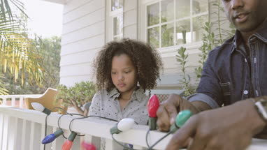 African American father and daughter hanging christmas lights outdoors