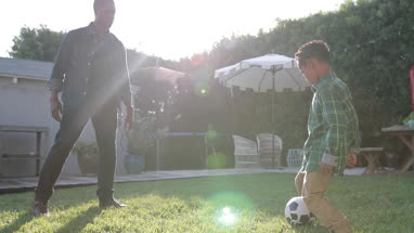 African American father and son playing football in yard