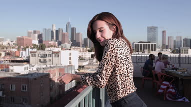 Young adult female looking out across city at a rooftop party