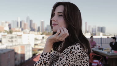 Young adult female looking out across city at a rooftop party and then smiling to camera