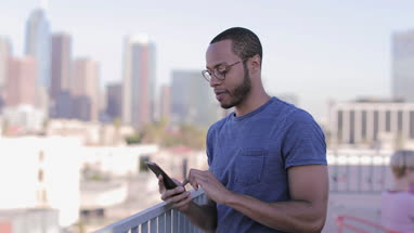 Young adult male taking photo of skyline with smartphone at a rooftop party