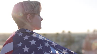 Young adult female wrapped in American flag looking out across city skyline