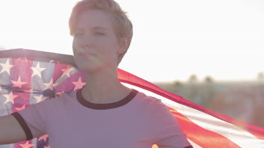 Young adult female holding out American flag looking out across city skyline