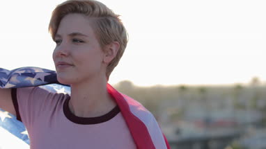 Young adult female holding out American flag looking out across city skyline